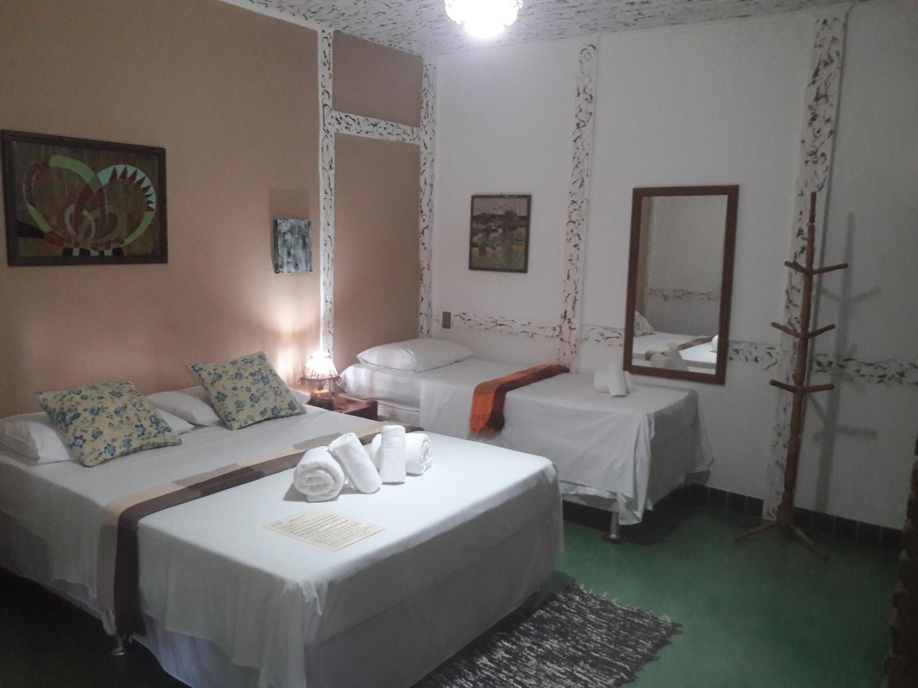 Hotellihuone, jossa on kaksi sänkyä, peili ja vihreä matto.