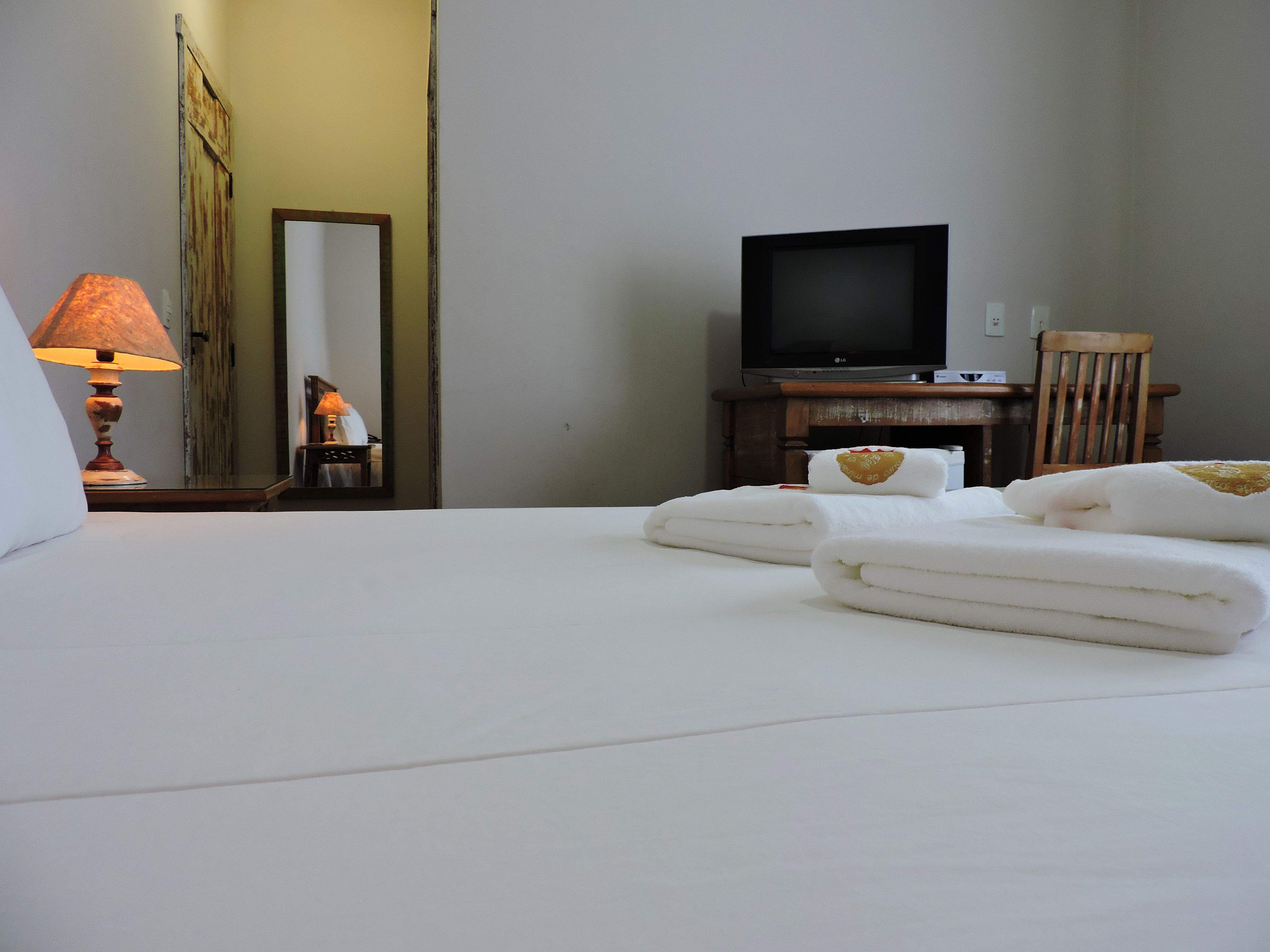 Una habitación de hotel con una cama bien hecha, un televisor sobre un mueble de madera y una lámpara en una mesita de noche.