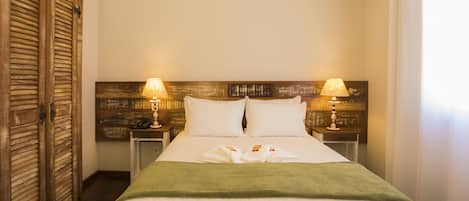 A hotel room with a bed, two bedside lamps, a wooden headboard, and a green throw blanket.