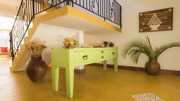 Un escalier avec une rampe noire, une console verte avec des tiroirs, un grand vase contenant des fleurs séchées et une plante en pot.