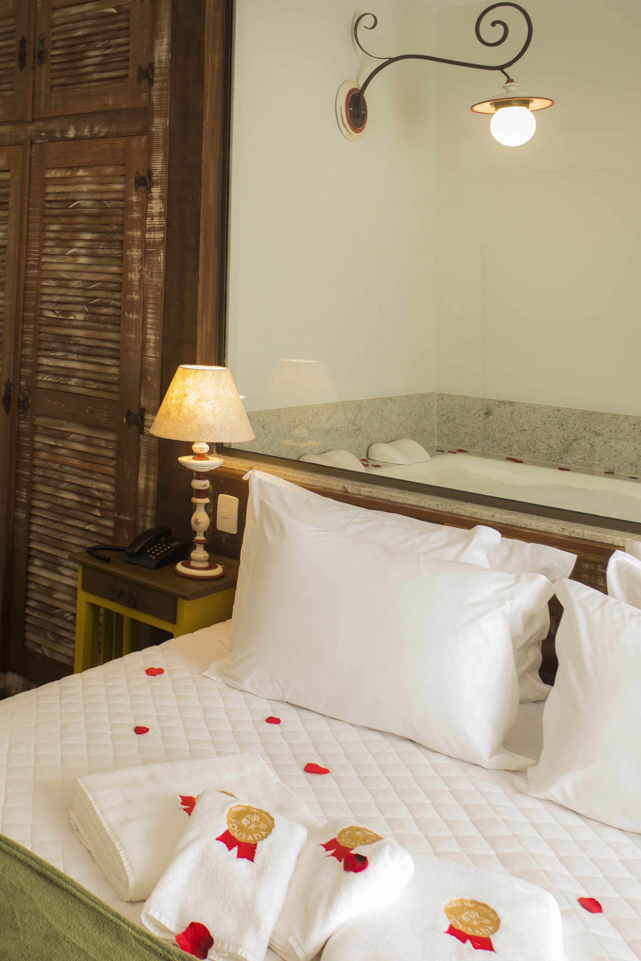 A hotel room with a bed, a nightstand with a lamp, a telephone, and a mirror above the bed.