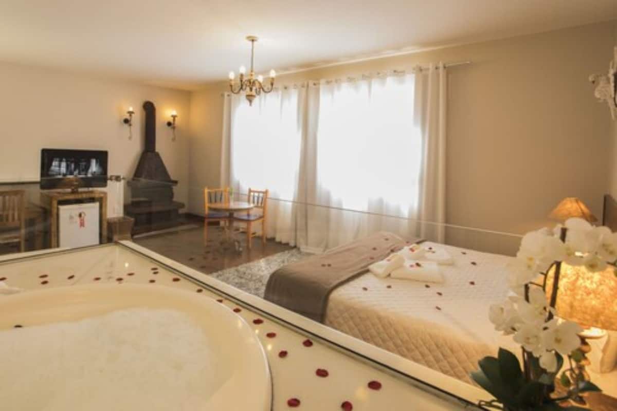 Ein Hotelzimmer mit einem Bett, einer Sitzecke mit einem Sessel, einem Kamin, einem Fernseher und einem großen Fenster mit Vorhängen.