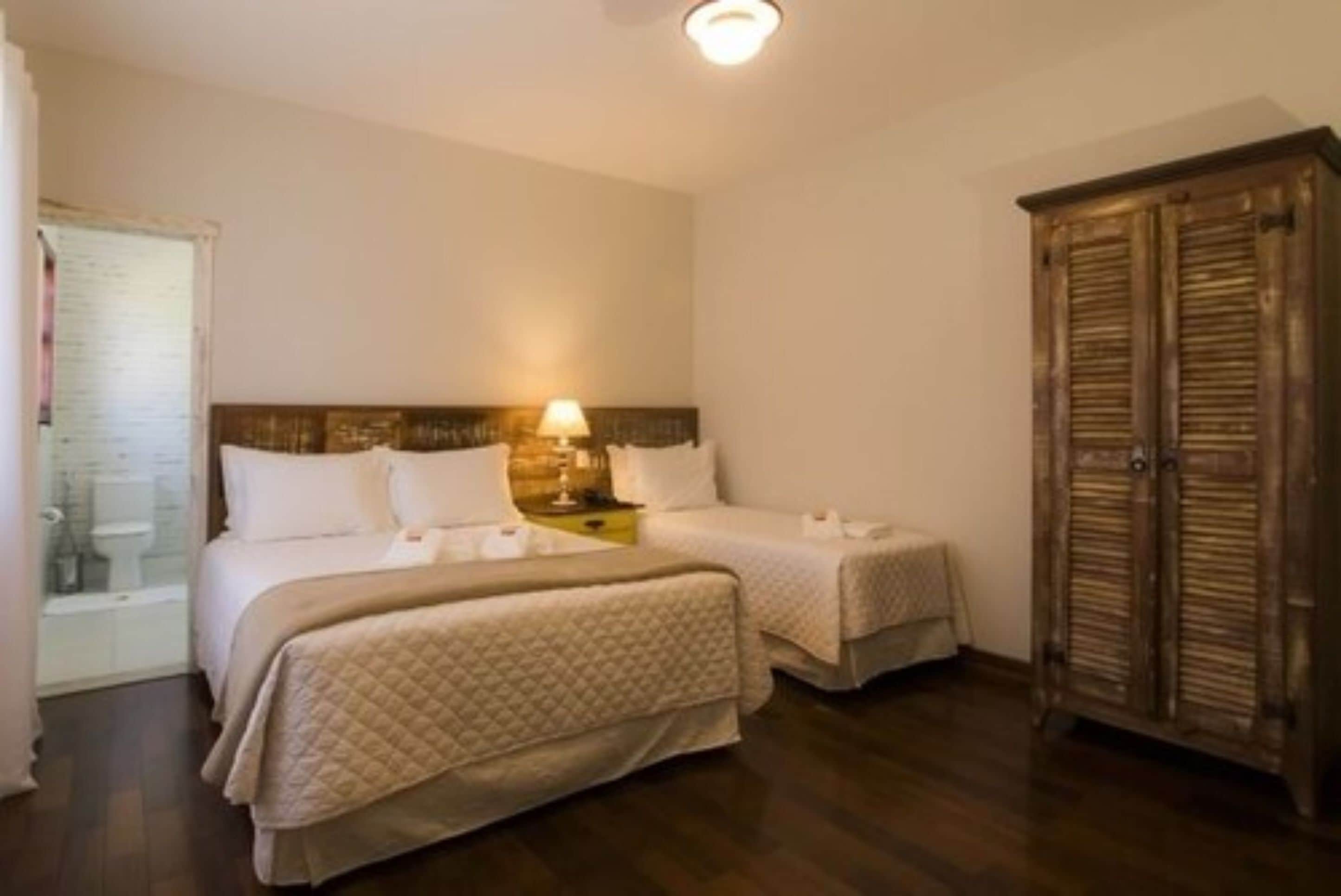 Une chambre d’hôtel avec deux lits, une armoire en bois et une table de chevet avec une lampe.