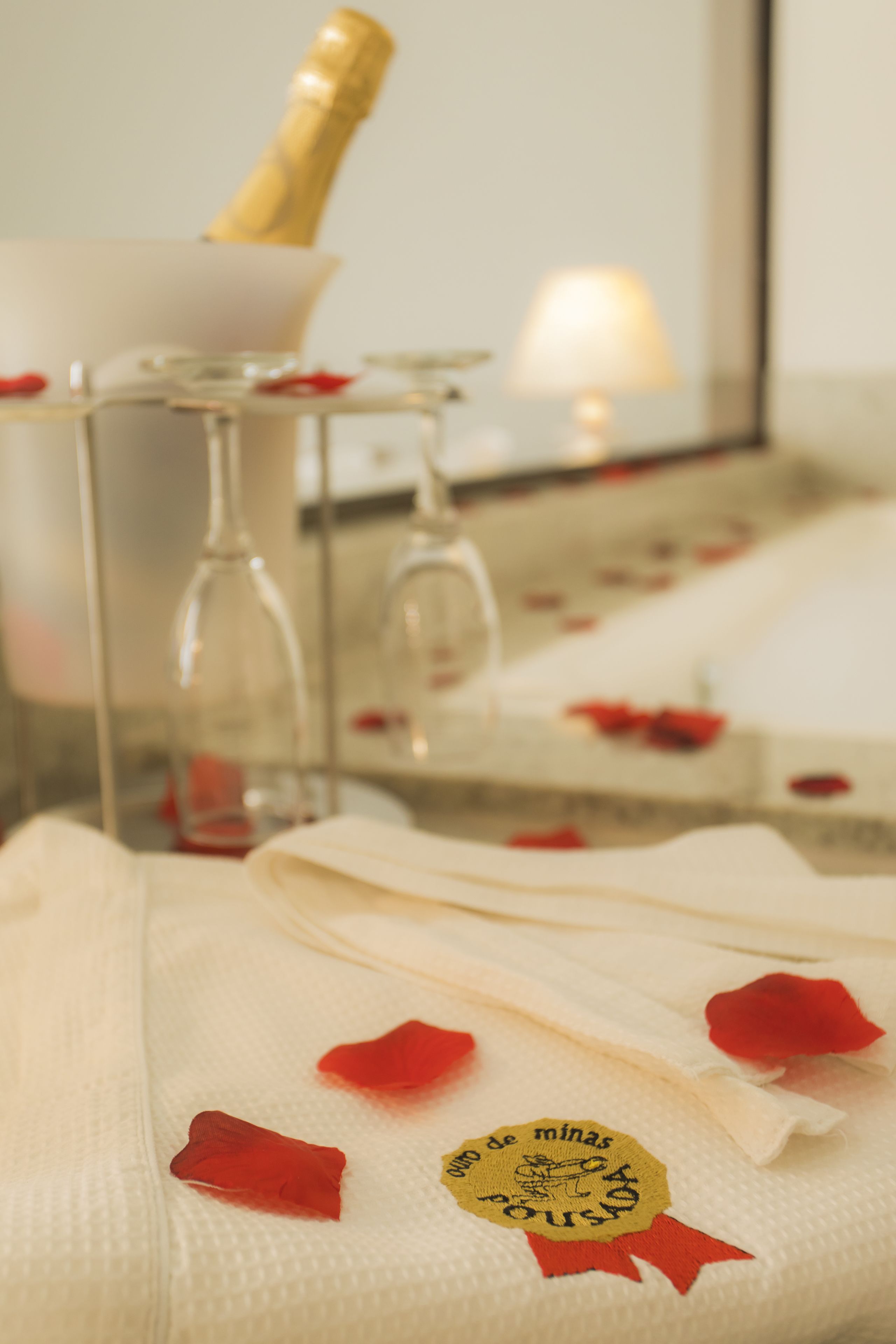 A close-up of a white towel with a gold emblem and red rose petals on a bed.