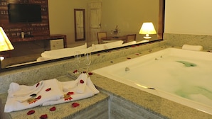Un baño de hotel con una bañera grande, un espejo, un lavabo y un televisor montado en la pared.