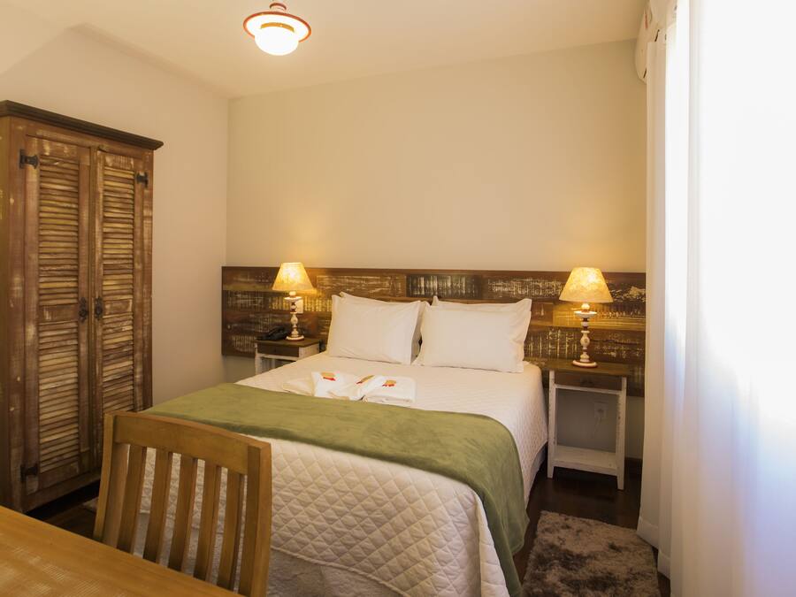 A bedroom with a bed, two bedside lamps, a wooden wardrobe, and a chair.