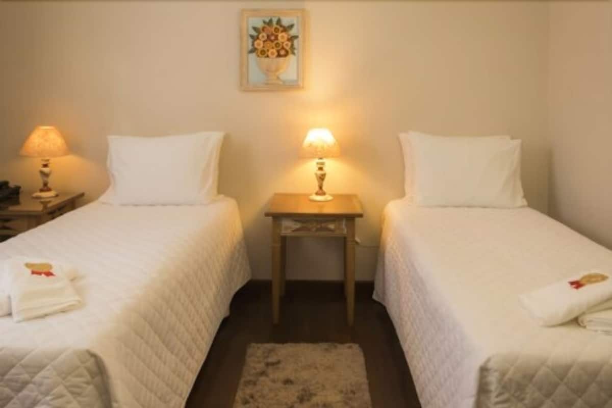 Ein Hotelzimmer mit zwei Einzelbetten, einem kleinen Tisch dazwischen und einem Nachttisch an jeder Seite.