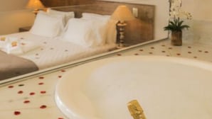 Un dormitorio con una bañera grande, una cama con ropa blanca y una botella de champán sobre una bandeja.
