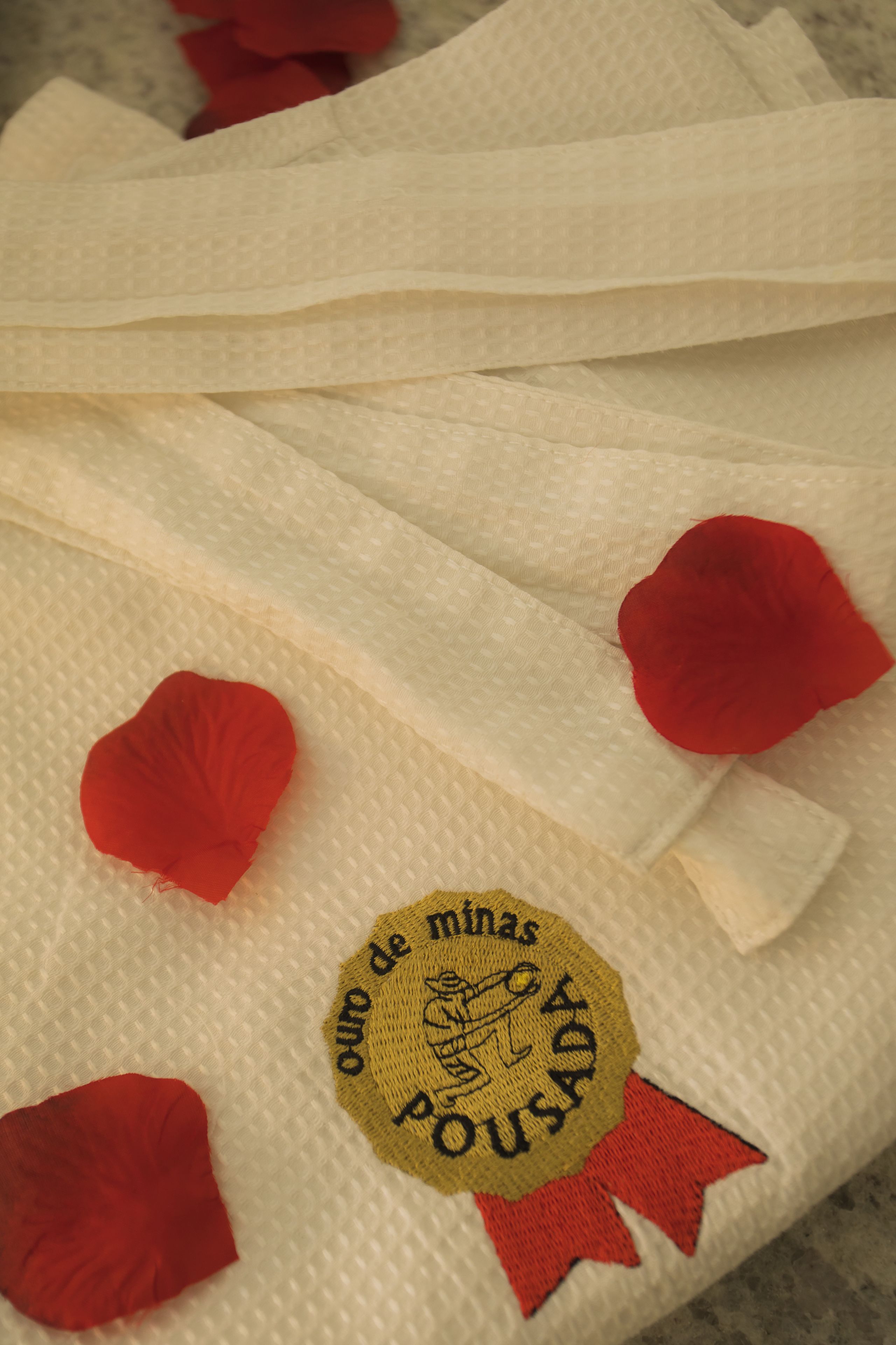 Toalla blanca con decoraciones en forma de corazón rojo y un emblema dorado con texto.