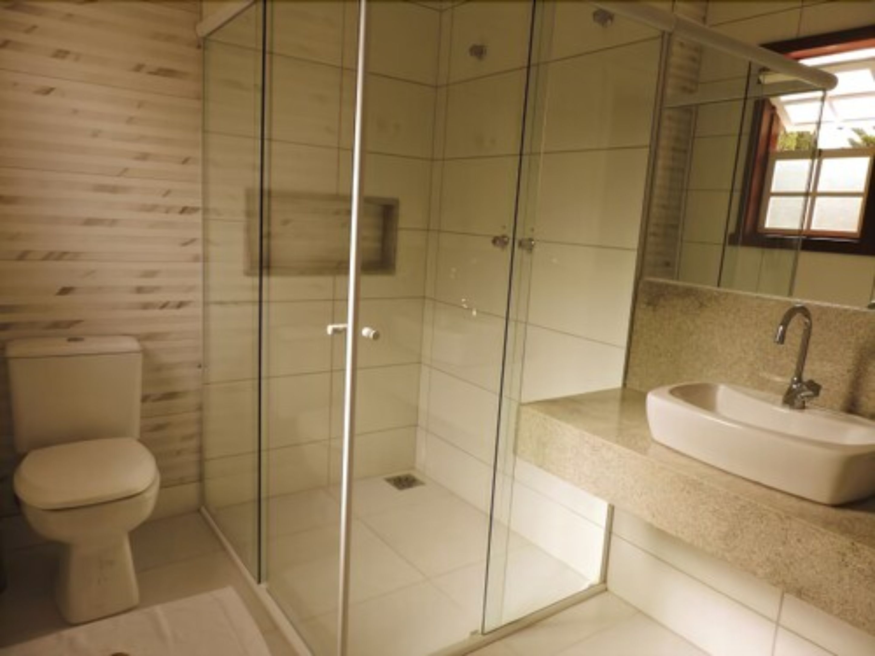 A bathroom with a glass-enclosed shower, a toilet, and a sink with a mirror above it.