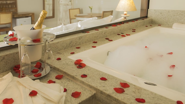 Un baño con una bañera, una botella de champán y pétalos de rosa en el suelo.