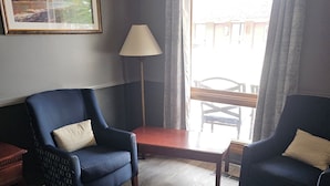A room with two dark blue armchairs, a wooden coffee table, a floor lamp, and a large window with curtains. - Blue Spruce Motel (North Platte)