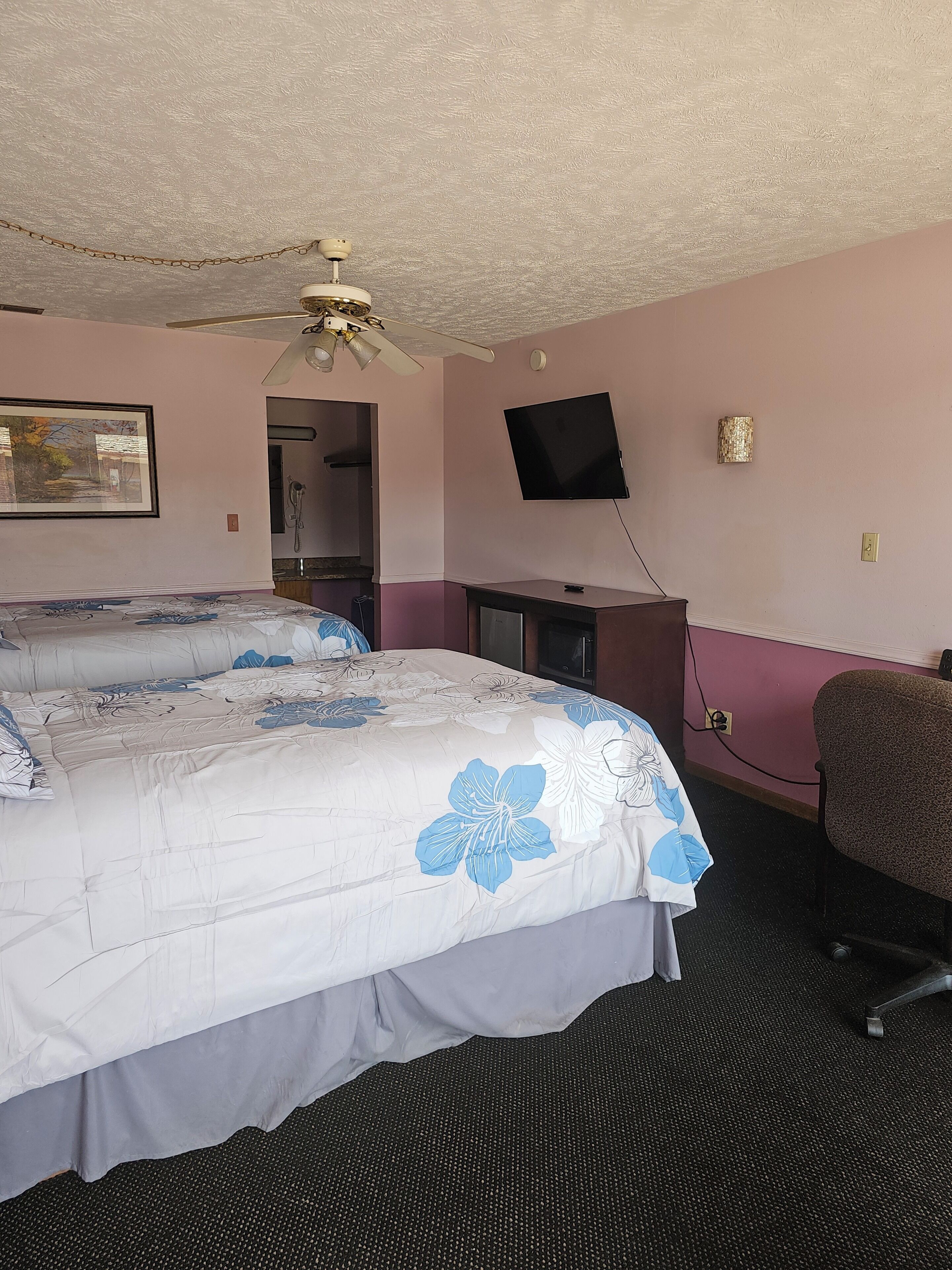 Habitación de hotel con dos camas, ventilador de techo, televisor y escritorio.