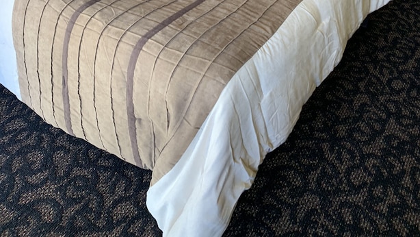 A hotel room with two beds, each with a striped bedspread, a wooden headboard, and a nightstand with a lamp. - Blue Spruce Motel (North Platte)