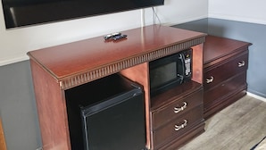 A wooden entertainment center with a flat-screen TV mounted above it, a small built-in TV, and a microwave drawer. - Blue Spruce Motel (North Platte)