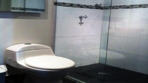 A bathroom with a toilet, a glass shower enclosure, and a tiled wall. - Apartamento Quinta Paredes 036 (Bogotá)