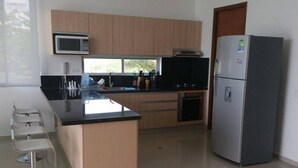 A modern kitchen with wooden cabinets, a stainless steel refrigerator, and a black countertop. - Apartamentos Puerto Valero 008 (Coveñas)