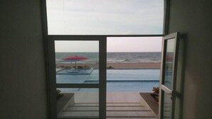 A view from a room with a glass door leading to a pool area with a red umbrella. - Apartamentos Puerto Valero 008 (Coveñas)