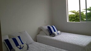 A room with two single beds, each with a pillow featuring a blue and white striped pattern and an anchor design. - Apartamentos Puerto Valero 008 (Coveñas)