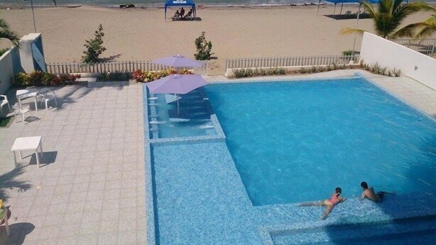 A pool area with a view of the beach, a shaded seating area, and a lifeguard station. - Apartamentos Puerto Valero 008 (Coveñas)