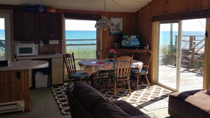 A cozy room with a wooden ceiling, a ceiling fan, a dining table with chairs, a sofa, and a large window offering a view of the ocean. -  LAKE MICHIGAN BEACHFRONT! PRIVATE BEACHFRONT! DISCOUNTED SEASONAL RATES  (Montague)