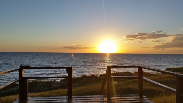 A wooden deck leading to a beach with a sunset in the background. -  LAKE MICHIGAN BEACHFRONT! PRIVATE BEACHFRONT! DISCOUNTED SEASONAL RATES  (Montague)