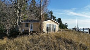 A small, single-story building with a door and windows, surrounded by tall grass and trees. -  LAKE MICHIGAN BEACHFRONT! PRIVATE BEACHFRONT! DISCOUNTED SEASONAL RATES  (Montague)