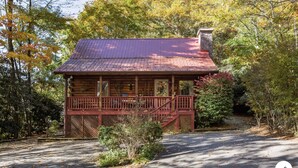 A log cabin with a porch, surrounded by trees and a stone chimney.