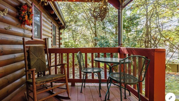 A wooden cabin with a porch featuring a rocking chair, two metal chairs, and a small table.