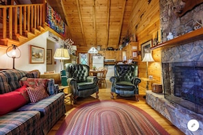 Interior acogedor de una cabaña de troncos con chimenea, dos sillones de cuero, un sofá a cuadros y un comedor.