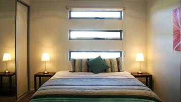 Una habitación de hotel con una cama grande, dos mesitas de noche con lámparas y tres ventanas.