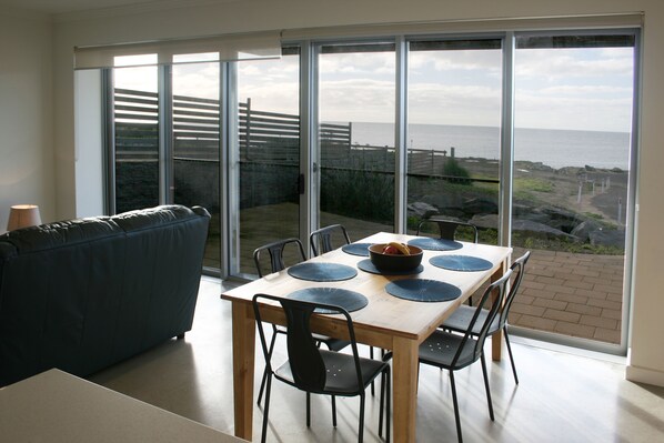 A dining area with a table set for four, a blue sofa, and a view of the sea through large sliding glass doors.