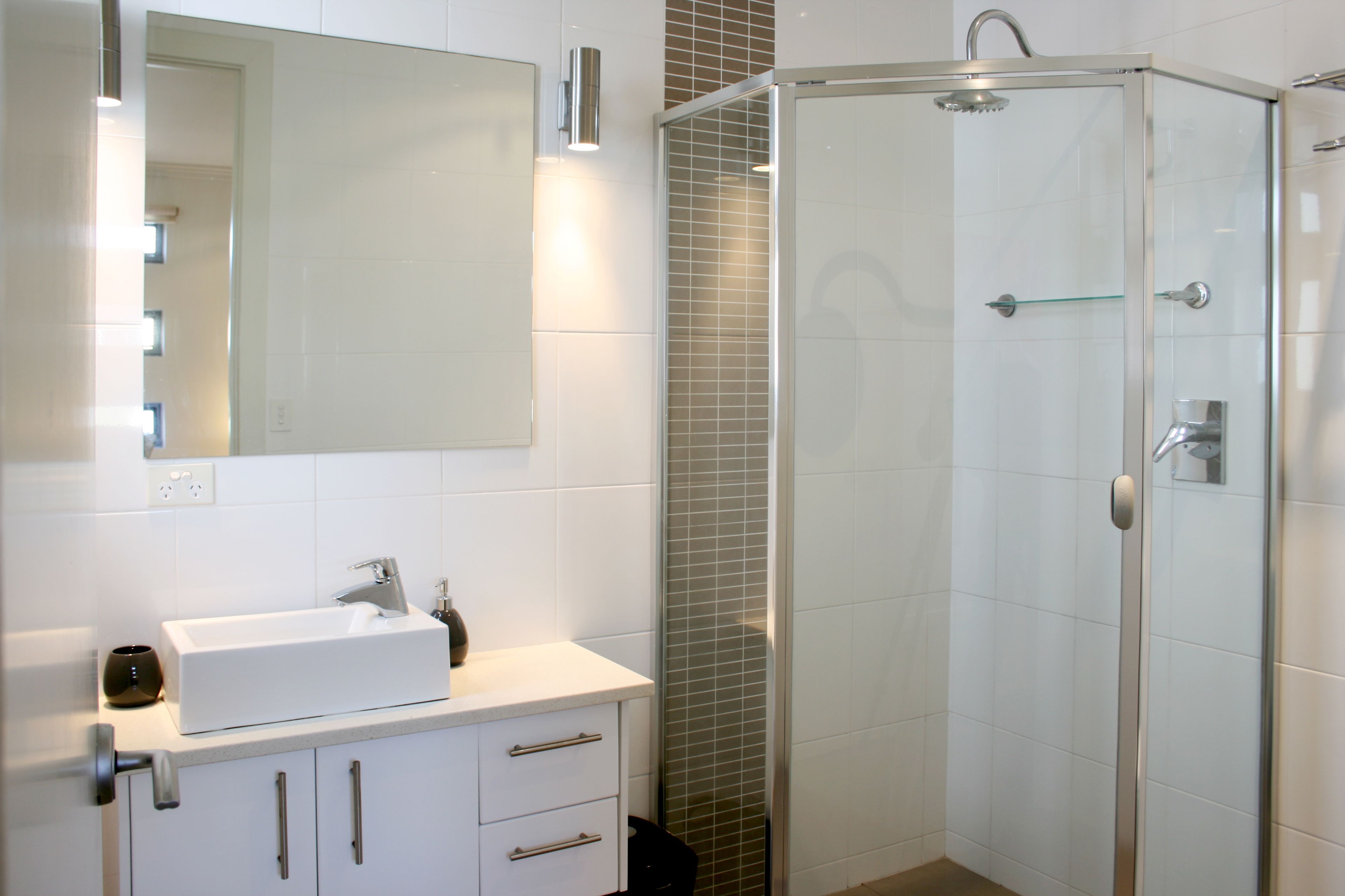 Un baño moderno con ducha de vidrio, un lavamanos blanco y un espejo sobre el mueble.