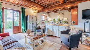 Un salon chaleureux avec un canapé, un fauteuil et une table basse. On aperçoit une cuisine à l’arrière-plan, avec un réfrigérateur et un coin repas.