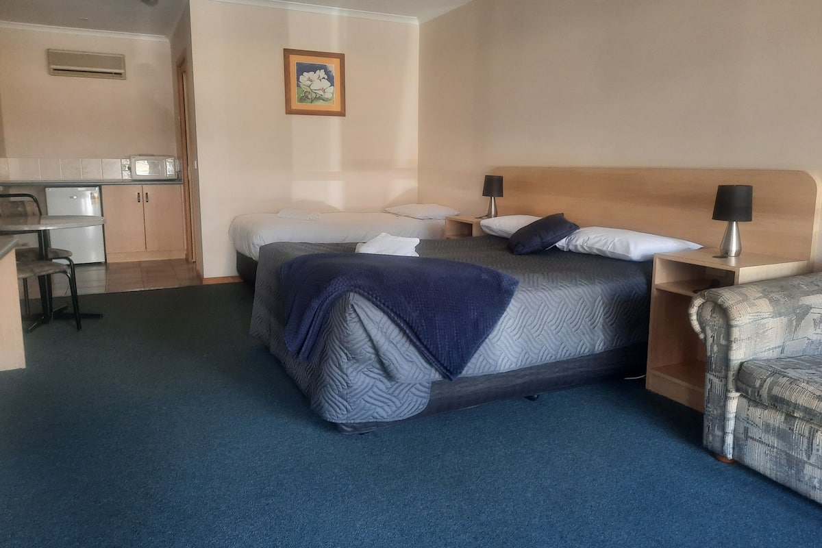 A hotel room with a bed, bedside tables, a desk, and a kitchenette.