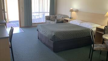 A hotel room with a large bed, a desk with a chair, a small table with a chair, and a window with curtains.