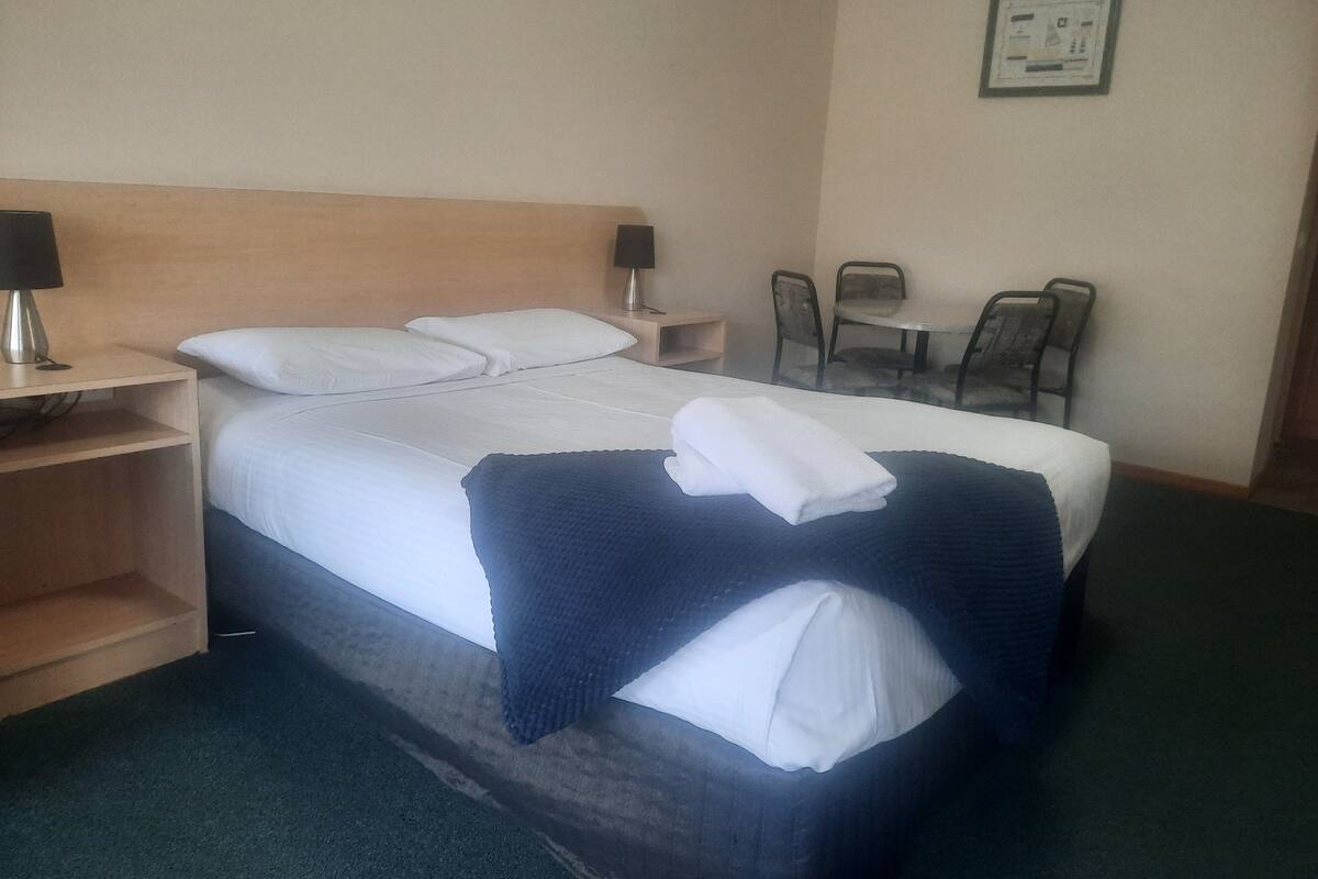 A hotel room with a bed, two bedside tables, a chair, and a small table.