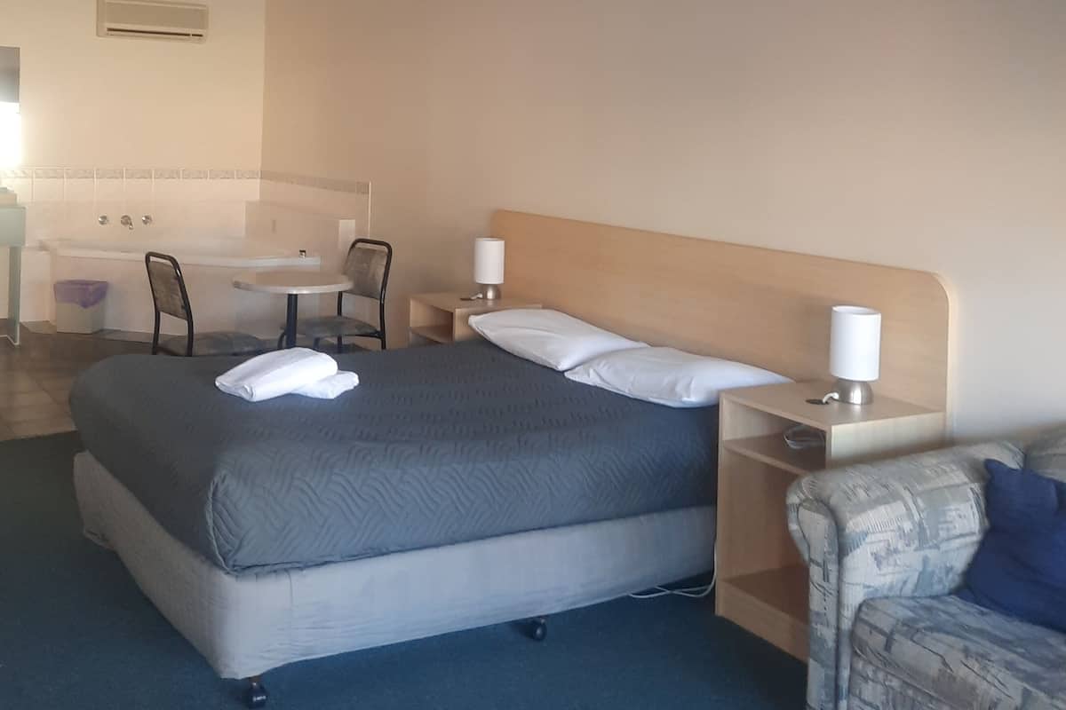 A hotel room with a bed, bedside tables, a chair, a small table, and a bathroom in the background.