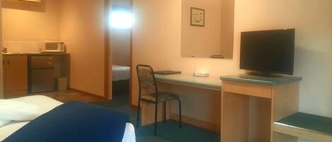 A hotel room with a bed, a desk with a computer, a television, a microwave, and a small kitchenette.
