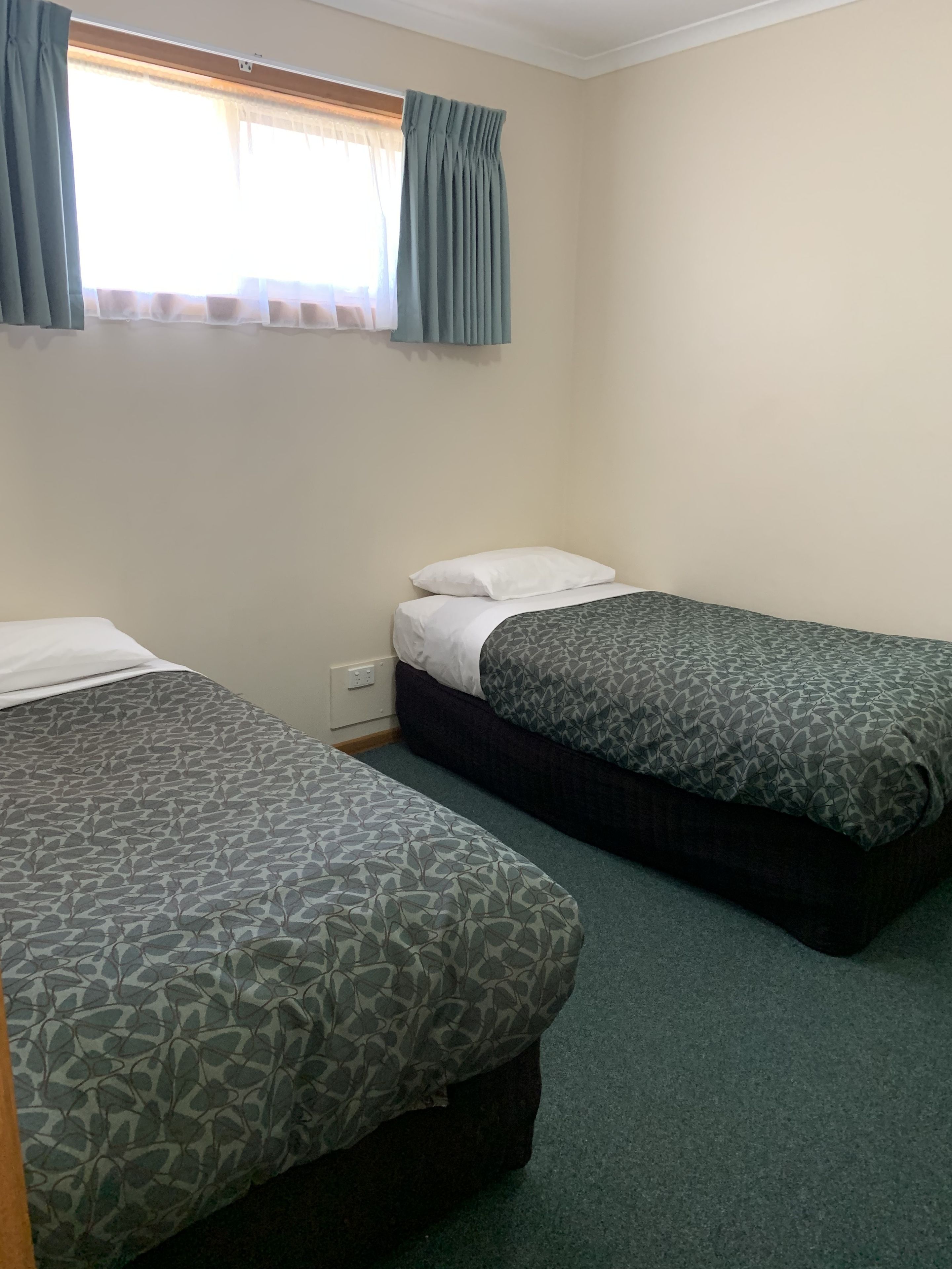 A room with two single beds, a window with curtains, and a plain wall.