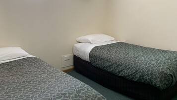 A room with two single beds, a window with curtains, and a plain wall.