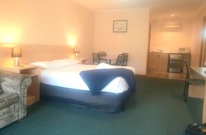 A hotel room with a bed, a desk, a chair, a small table, and a kitchenette.