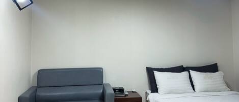 A room with a bed, a sofa, a small table, and a nightstand.