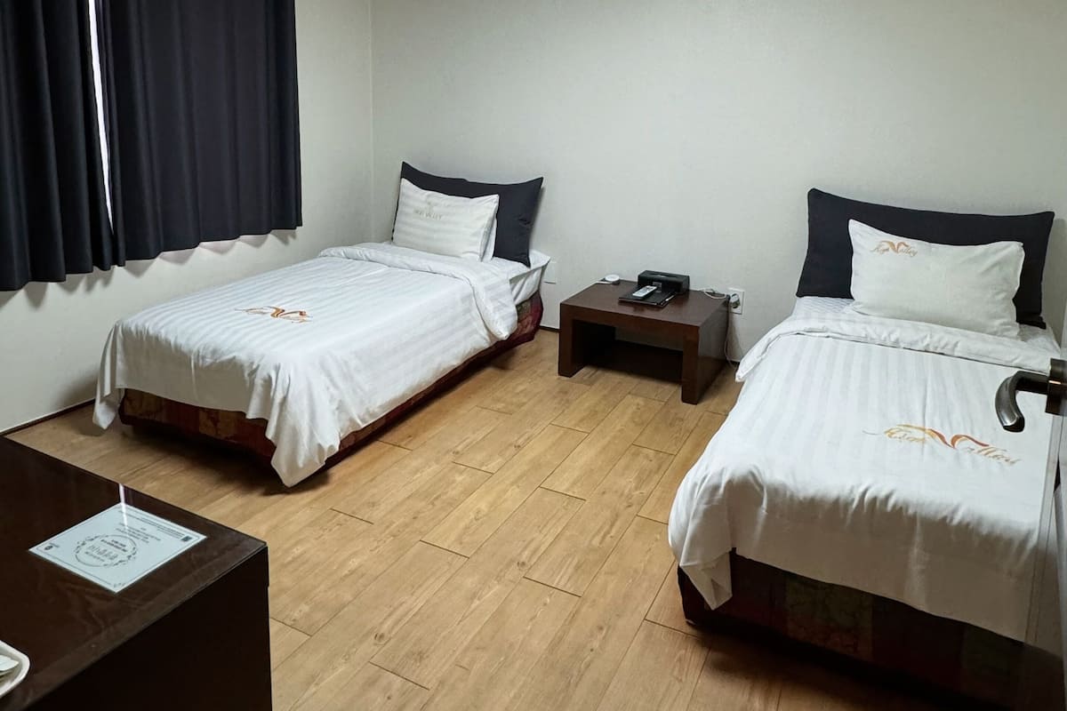 Une chambre d’hôtel avec deux lits, un bureau, une table de chevet et un luminaire au plafond.