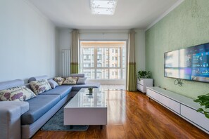 A modern living room with a sofa, coffee table, and a TV on the wall. - Bliss Guesthouse (Xi'an)