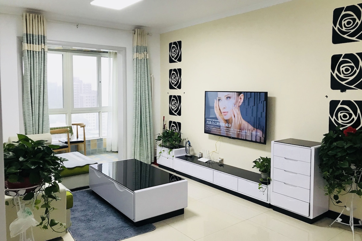 A modern living room with a sofa, a TV mounted on the wall, a cabinet, and a window with curtains.