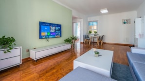 Ein modernes Wohnzimmer mit Flachbildfernseher, Holzboden, einem weißen Sofa und einem Couchtisch.