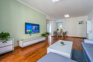 A modern living room with a flat-screen TV, wooden flooring, a white sofa, and a coffee table. - Bliss Guesthouse (Xi'an)