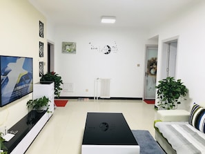 A modern living room with a flat-screen TV, a black coffee table, a sofa, and a large window. - Bliss Guesthouse (Xi'an)