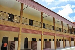A multi-story hotel with balconies, a covered walkway, and a row of rooms with shutters.